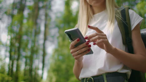 Close-up-of-a-mobile-phone-in-the-hands-of-a-female-traveler-walking-through-the-forest.-Social-networks-Navigator-and-messenger.-Use-your-mobile-phone-for-a-walk-in-the-woods